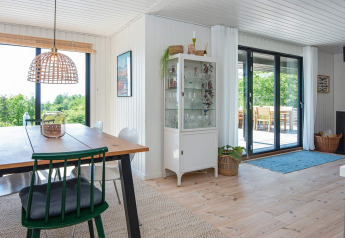 Bright dining area in an 8-person holiday home in Ebeltoft, Denmark, with large windows and wooden furniture.