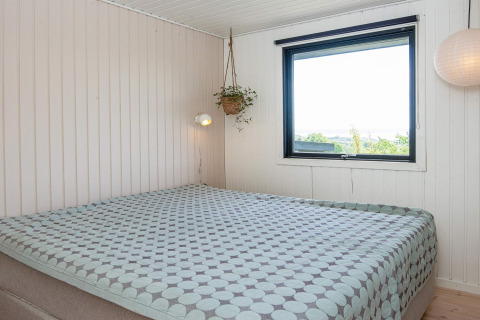 Slaapkamer met tweepersoonsbed, modern interieur, groot raam en hangplant in een vakantiehuis in Ebeltoft.