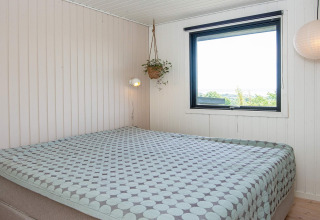 Dormitorio con cama doble, decoración moderna, gran ventana y planta colgante en una casa de vacaciones en Ebeltoft.