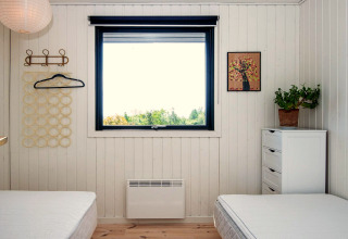 Chambre avec deux lits, fenêtre vue nature, commode blanche, plante et tableau mural à Ebeltoft.