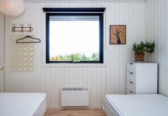 Chambre avec deux lits, fenêtre vue nature, commode blanche, plante et tableau mural à Ebeltoft.