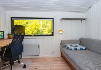 Moderne werk- en zithoek met groot raam, bureau, stoel en slaapbank in een vakantiehuis in Ebeltoft, Denemarken.