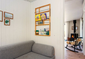 Salon d'une maison de vacances à Ebeltoft avec canapé gris, œuvres murales et poêle à bois au fond.