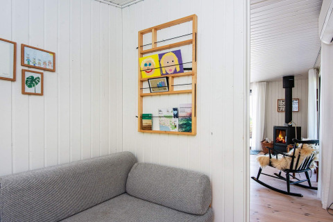 Stue i et feriehus i Ebeltoft med grå sofa, kunst på væggen og pejs i baggrunden.