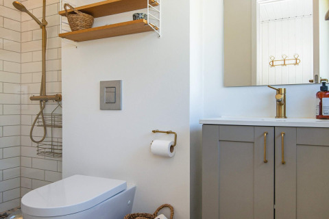 Moderne badkamer met douche, toilet, wastafel en gouden kraan in een vakantiehuis in Ebeltoft, Denemarken.