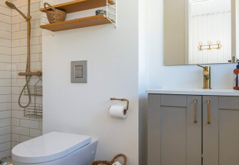Moderne badkamer met douche, toilet, wastafel en gouden kranen in een vakantiehuis in Ebeltoft, Denemarken.