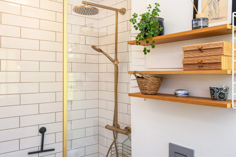 Moderne badkamer met messingdouche, witte tegels en houten planken met planten en decoratie.