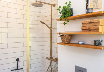 Moderne badkamer met messing douche, witte tegels en houten planken met planten en decoratie.