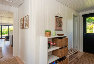 Entrée d'une maison de vacances à Ebeltoft avec murs en panneaux blancs, paniers en osier et vue sur le salon.