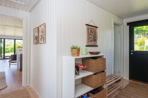Entrée d'une maison de vacances à Ebeltoft avec murs en panneaux blancs, paniers en osier et vue sur le salon.