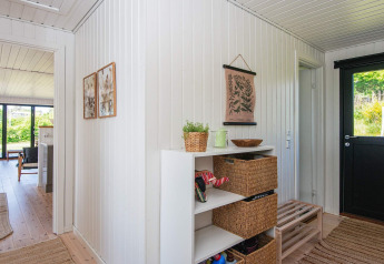 Entryway in an Ebeltoft holiday home featuring white panel walls, wicker storage, and access to the living room.