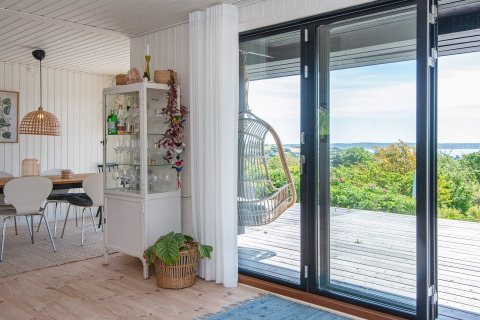 Living room in Ebeltoft holiday home with glass doors to terrace, hanging chair and dining area.
