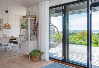 Stue i feriebolig i Ebeltoft med glasdøre til terrasse, hængestol, vitrineskab og spisebord.