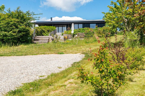 Udendørsbillede af 8-personers feriehus i Ebeltoft, Danmark, omgivet af grøn have og blå himmel.
