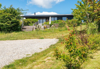 Udendørsbillede af 8-personers feriehus i Ebeltoft, Danmark, omgivet af grøn have og blå himmel.
