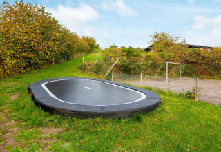 Trampolino interrato su prato verde vicino a una casa vacanze per 8 persone a Ebeltoft, Danimarca.