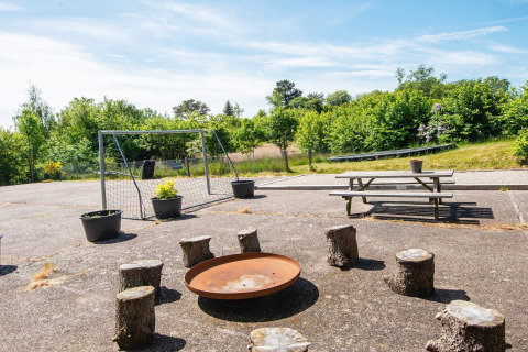 Outdoor area at 8 person holiday home in Ebeltoft, Denmark with fire pit, log seats, bench, and goal.