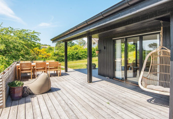 Sunny terrace at an 8-person holiday home in Ebeltoft, Denmark, featuring dining area and hanging chair.