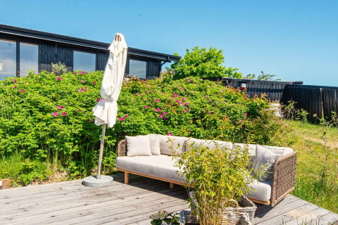 Terrasse extérieure avec canapé, parasol et verdure à la maison de vacances 8 personnes à Ebeltoft, Danemark.