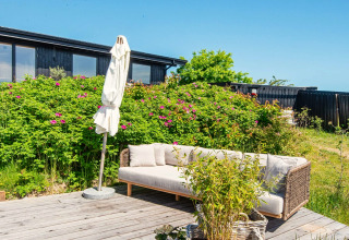 Terrasse extérieure avec canapé, parasol et verdure à la maison de vacances 8 personnes à Ebeltoft, Danemark.