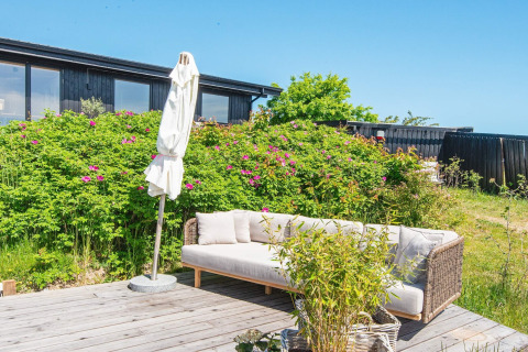 Terrazza esterna con divano, ombrellone e piante presso casa vacanze per 8 persone a Ebeltoft, Danimarca.