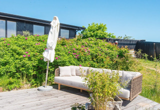 Terrasse mit Sofa und Sonnenschirm im 8-Personen-Ferienhaus in Ebeltoft, Dänemark, an einem sonnigen Tag.
