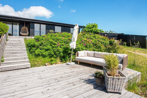 Holzterrasse mit Sofa und Pflanzen am 8-Personen-Ferienhaus in Ebeltoft, Dänemark, bei sonnigem Wetter.