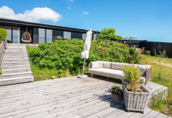 Houten terras met bank en planten bij 8-persoons vakantiehuis in Ebeltoft, Denemarken, met veel groen eromheen.