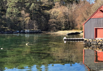 Casa rossa sul lago calmo circondato da boschi a Reksteren, Danimarca, con riflessi sull’acqua.