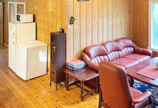 Sala de estar en casa vacacional en Reksteren, Dinamarca, con sofá de cuero, mesa, nevera y microondas.