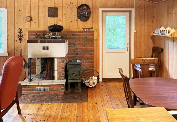 Accogliente interno di una casa vacanza a Reksteren, Danimarca, con camino, pareti in legno e zona pranzo.