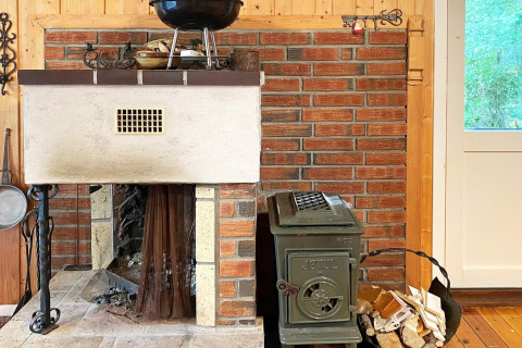 Gemütliche Kamin- und Holzofenecke in einer Berghütte in Reksteren, Dänemark, mit gestapeltem Holz.