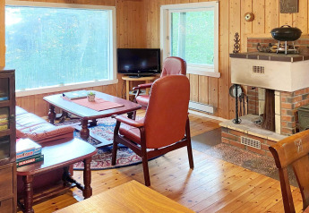 Salotto in legno con camino, poltrone in pelle, grande finestra e giochi da tavolo nel lodge Reksteren.