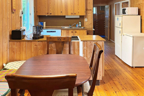 Cucina e zona pranzo in una baita di legno con tavolo, sedie e elettrodomestici a Reksteren, Danimarca.
