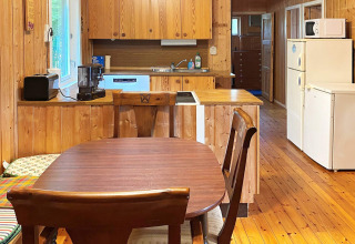 Keuken en eetgedeelte van een houten lodge met tafel, stoelen en apparaten in Reksteren, Denemarken.