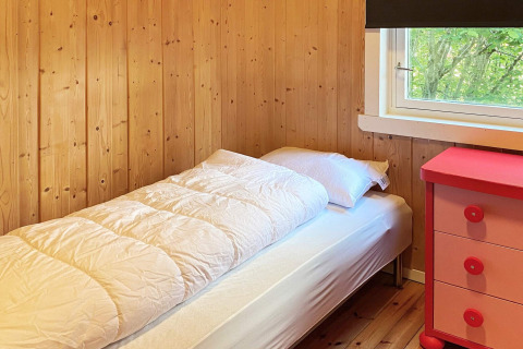 Camera accogliente con letto singolo, pareti in legno, finestra e cassettiera rossa in un lodge a Reksteren.