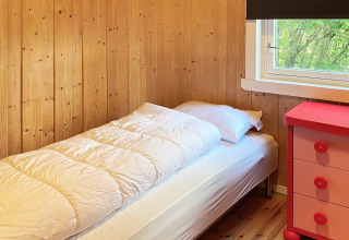 Gemütliches Schlafzimmer mit Einzelbett, Holzwänden, Fenster und roter Kommode in Reksteren, Dänemark.