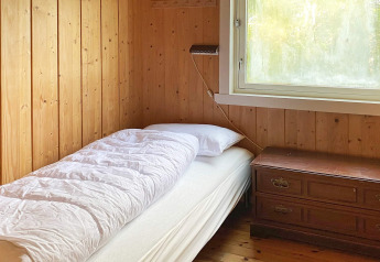Knusse slaapkamer met eenpersoonsbed, wit beddengoed, houten wanden, raam en houten ladekast.
