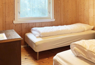 Camera da letto con due letti singoli, pareti in legno e ampia finestra in una casa vacanze a Reksteren, Danimarca.