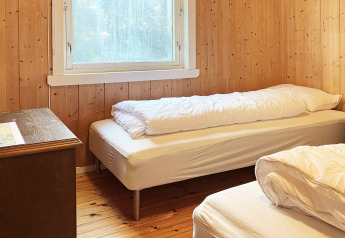 Slaapkamer met twee eenpersoonsbedden, houten wanden en raam in een vakantiehuis in Reksteren, Denemarken.