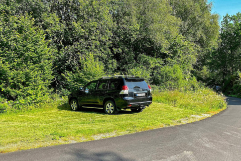 SUV nero parcheggiato sull’erba vicino alla strada e circondato da alberi presso casa vacanze a Reksteren.