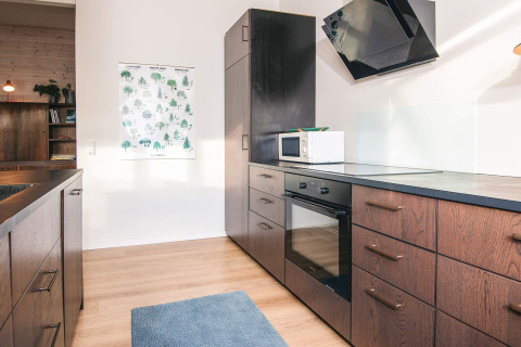 Moderne keuken met houten kasten, oven, magnetron en blauw vloerkleed in vakantiehuis in Ans By, Denemarken.