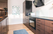 Cocina moderna con armarios de madera, horno, microondas y alfombra azul en una casa de vacaciones en Dinamarca.