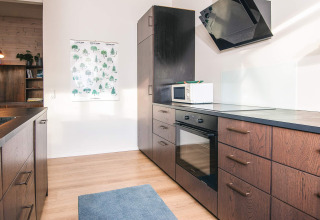 Cucina moderna con mobili in legno, forno, microonde e tappeto blu in una casa vacanze ad Ans By, Danimarca.