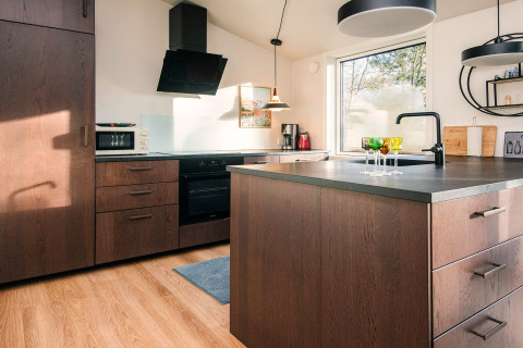 Cucina moderna con mobili in legno, isola centrale, grande finestra e luce naturale ad Ans By, Danimarca.