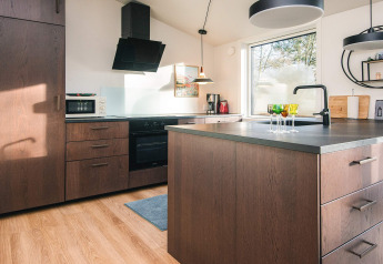 Cocina moderna con gabinetes de madera, isla, gran ventana y luz natural en Ans By, Dinamarca.