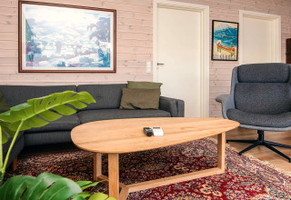 Stue i et feriehus i Ans By, Danmark, med grå sofa, lænestol, træbord og farverigt tæppe.