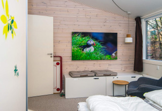 Knusse kamer in een vakantiewoning in Ans By, Denemarken, met groot raam, modern interieur en tv met papegaaiduiker.