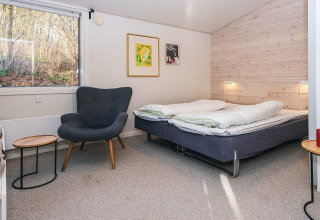 Chambre moderne dans un lodge avec lit double, fauteuil, décor mural et grande fenêtre à Ans By, Danemark.