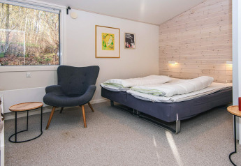 Moderne slaapkamer in een lodge met tweepersoonsbed, fauteuil, wandkunst en groot raam in Ans By, Denemarken.